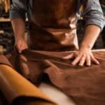 A craftsman wearing a leather apron working with eco-friendly leather in a sustainable leather workshop.