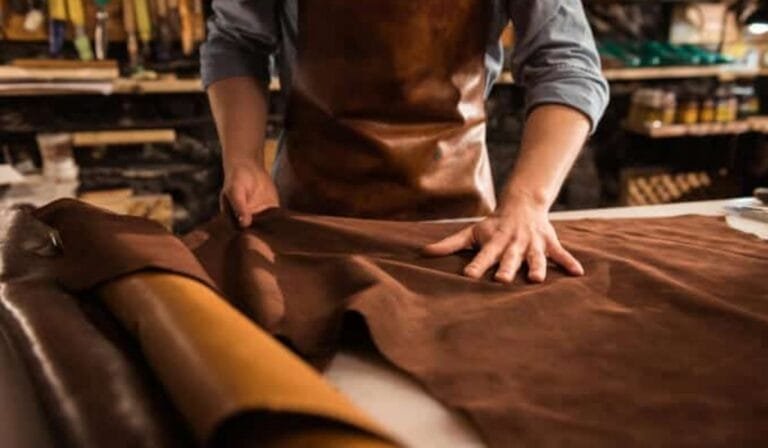 A craftsman wearing a leather apron working with eco-friendly leather in a sustainable leather workshop.