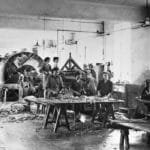 A historical leather tannery with workers processing hides using large tanning drums and traditional machinery.