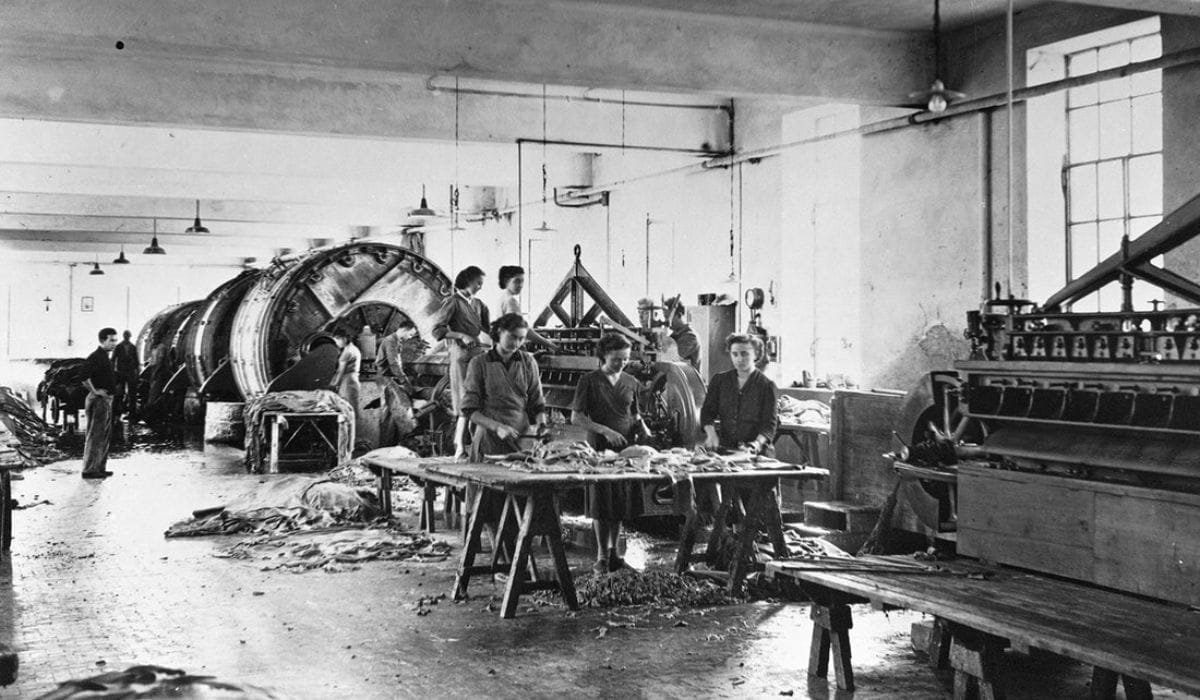 A historical leather tannery with workers processing hides using large tanning drums and traditional machinery.
