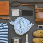 Flat lay of stylish leather travel accessories, including a brown leather bag, belt, wallet, and boots, along with other essentials.