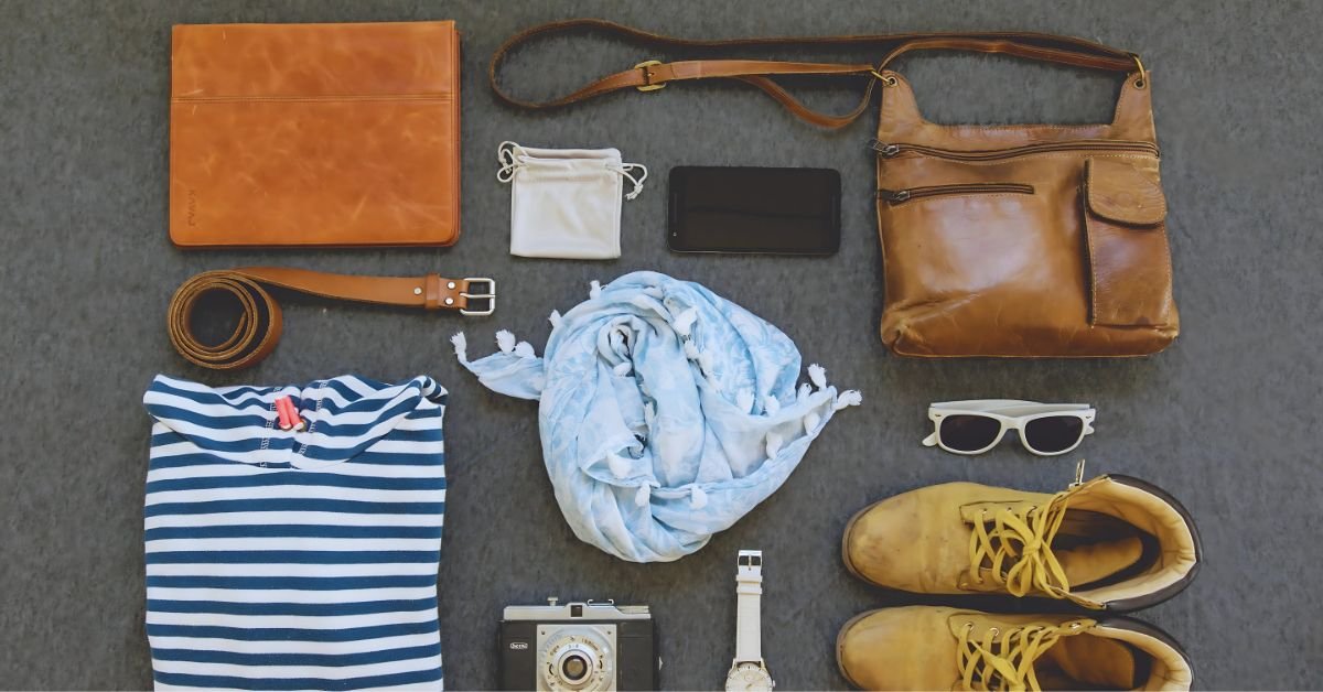 Flat lay of stylish leather travel accessories, including a brown leather bag, belt, wallet, and boots, along with other essentials.