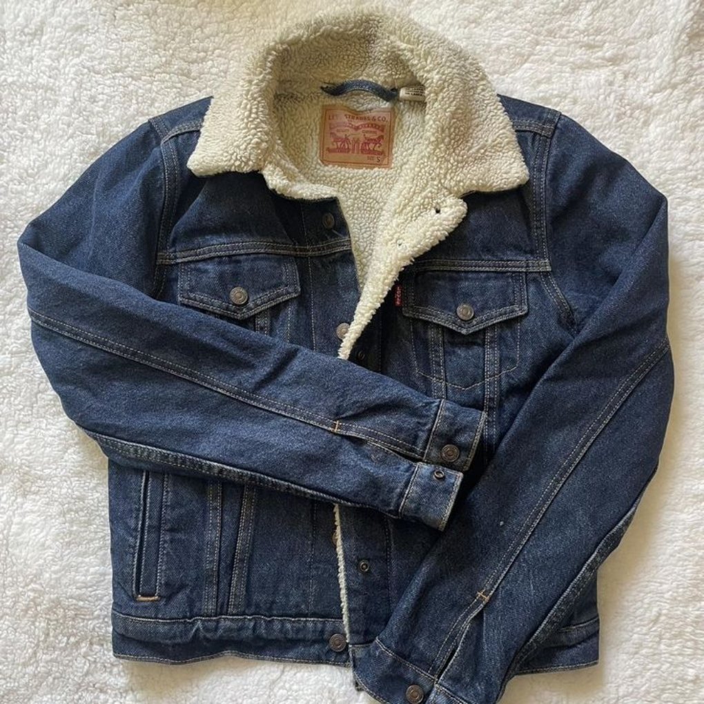 A denim jacket with a sherpa-lined collar laid flat on a soft surface.