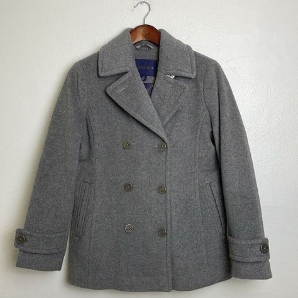 A gray double-breasted coat hanging on a hook against a plain wall.