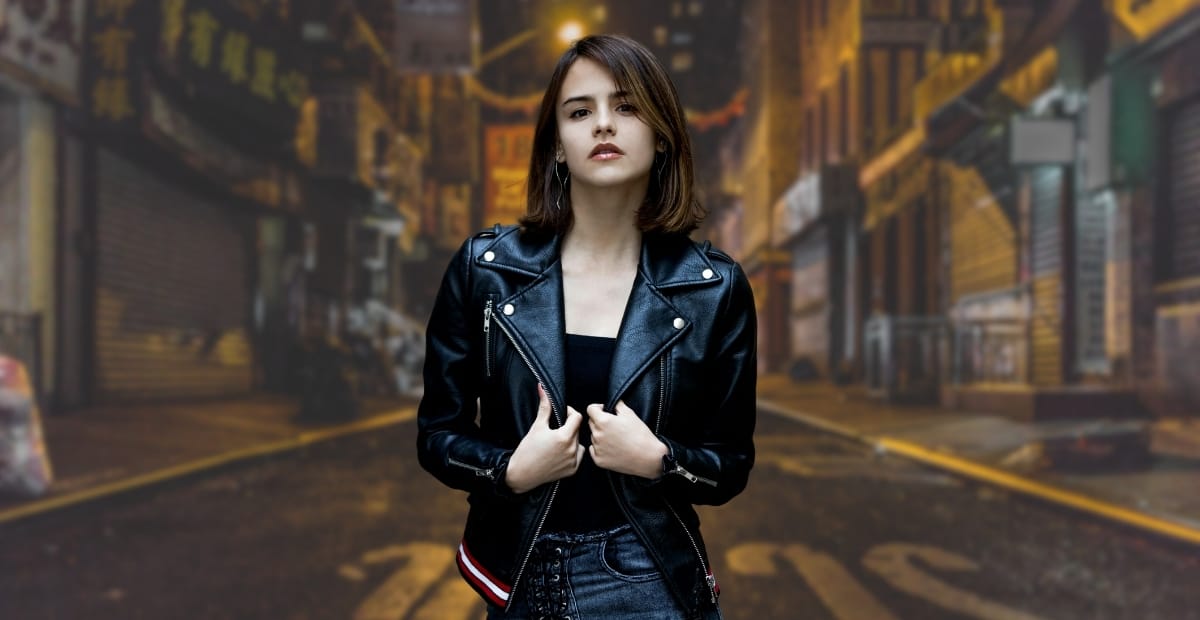 A-1 Bomber Jacket: The Timeless Style Staple You Need A young woman with shoulder-length brown hair, dressed in a black A-1 bomber jacket, standing on a dimly lit city street at night with blurred buildings and signs in the background.