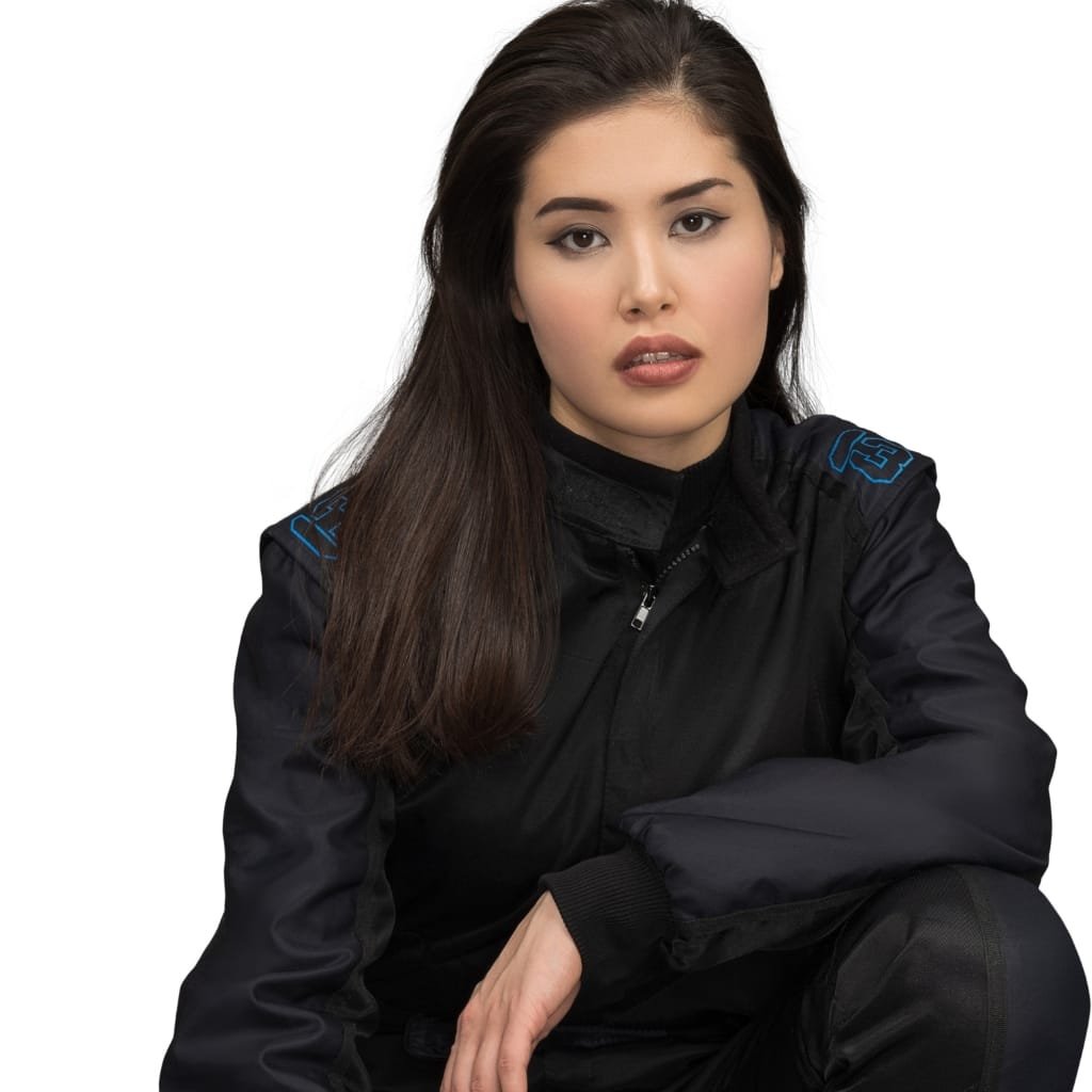 A woman with long dark hair, wearing a black aerodynamic jacket, sitting with her arm resting on her knee against a plain white background.