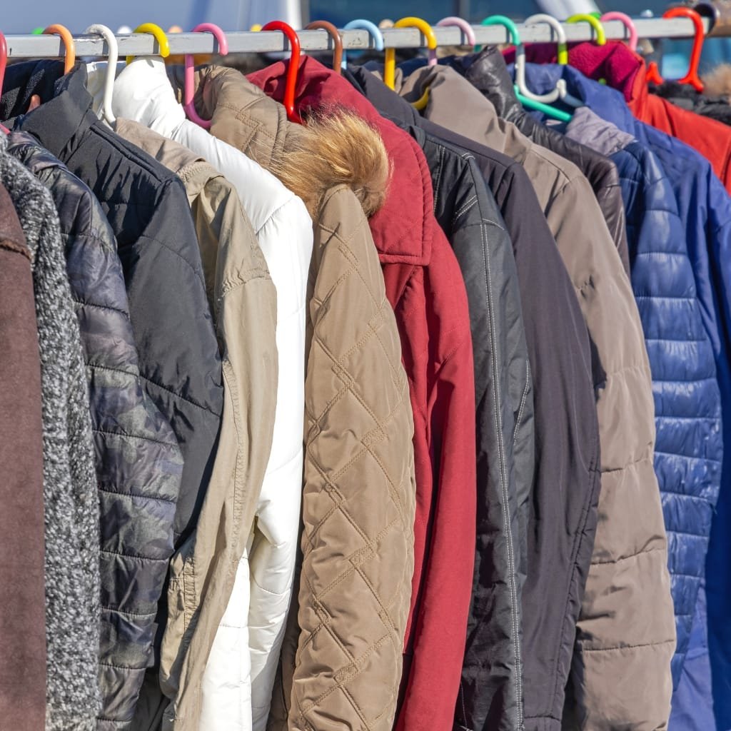 A row of various quilted jackets hanging on a clothing rack, showcasing different colors, styles, and fabrics.

