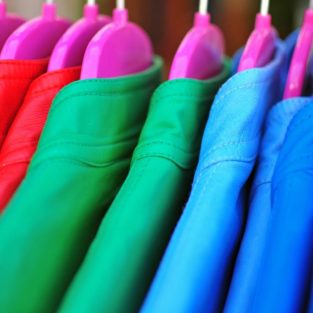 Close-up of colorful leather shirt jackets hanging on hangers, showcasing vibrant red, green, and blue colors with purple hangers.

