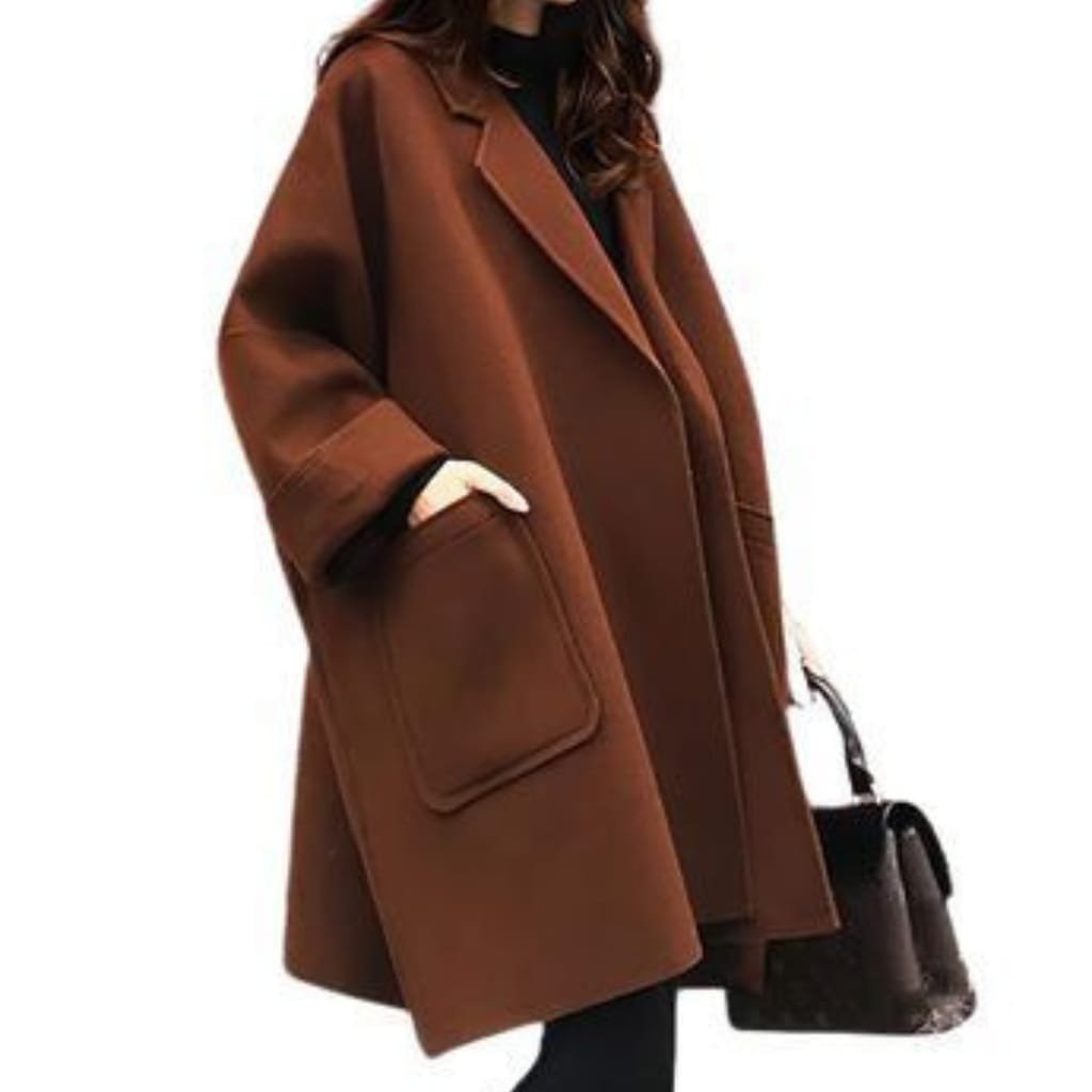 A stylish woman wearing a classic brown wool coat, paired with black pants and a black bag, standing against a plain white background.