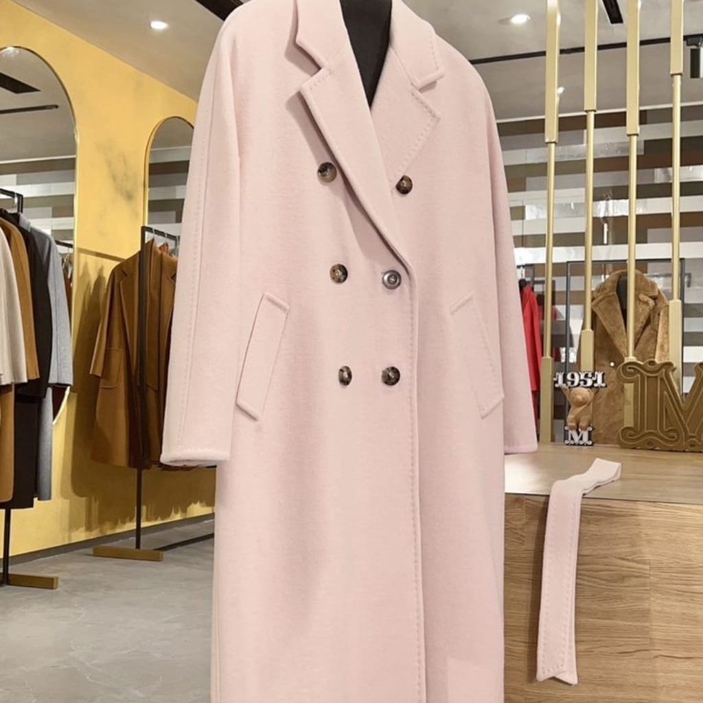 A soft pink women's wool coat with a double-breasted design, large lapels, and contrasting buttons, displayed on a mannequin inside a retail store.