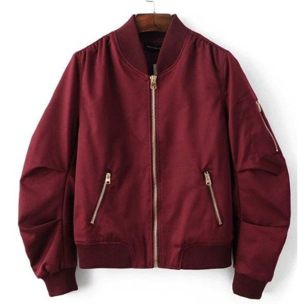 A stylish maroon bomber jacket with gold zippers, featuring ribbed cuffs, collar, and hem, hanging against a plain background.

