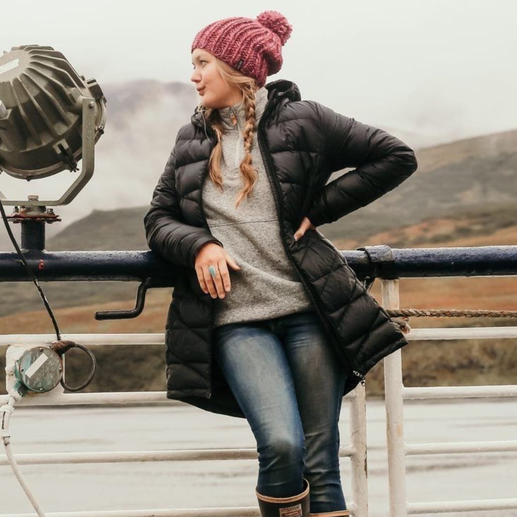 Woman in a black Alaska winter coat and knit hat standing on a ferry deck in cold weather.