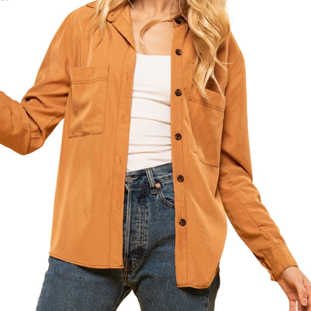 A woman wearing a classic button-up shirt jacket in light brown/tan color, paired with a white top and blue jeans.