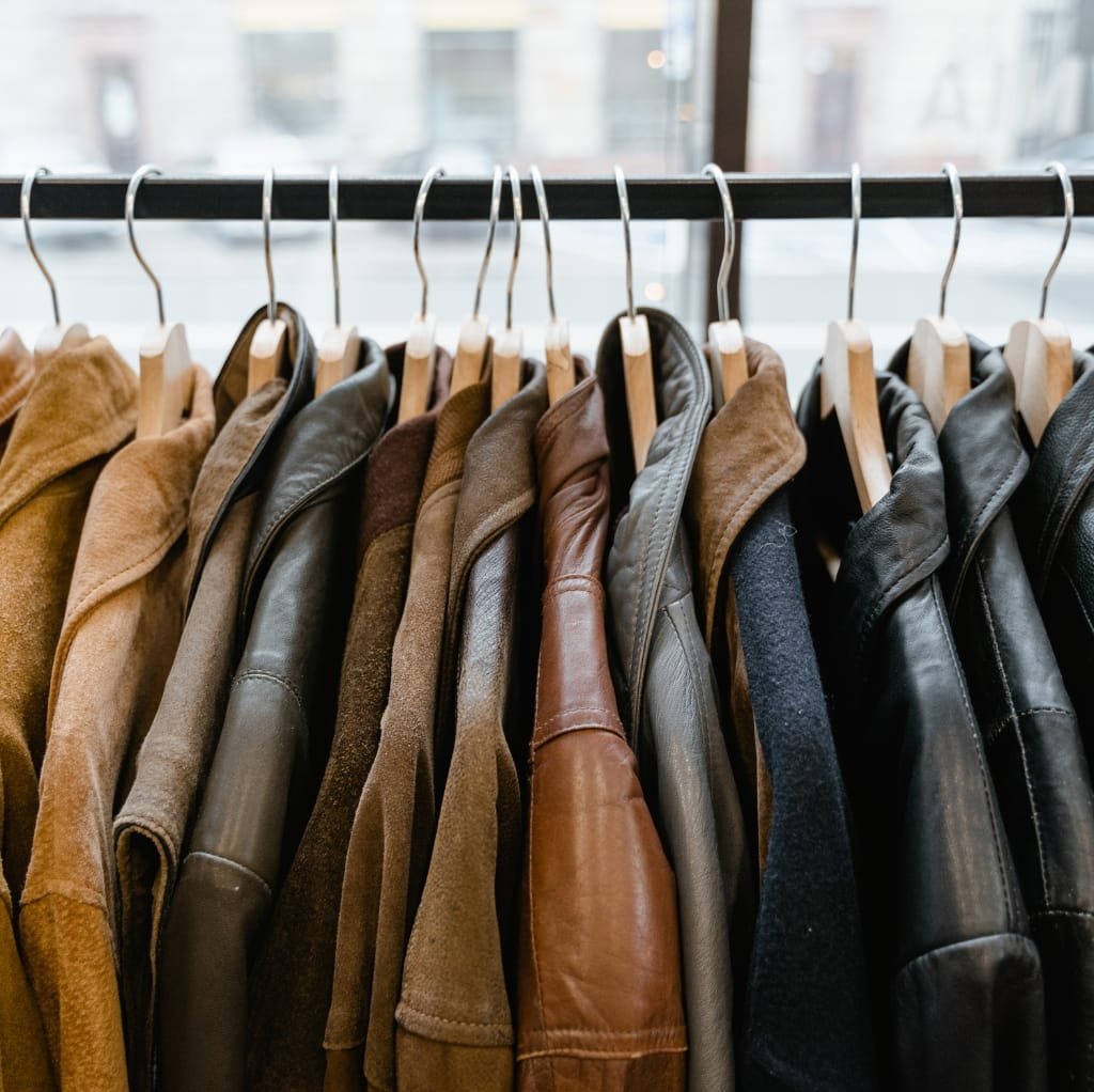 A row of classic jackets hanging on wooden hangers on a clothing rack, showcasing a variety of timeless colors including shades of brown, black, gray, and tan.