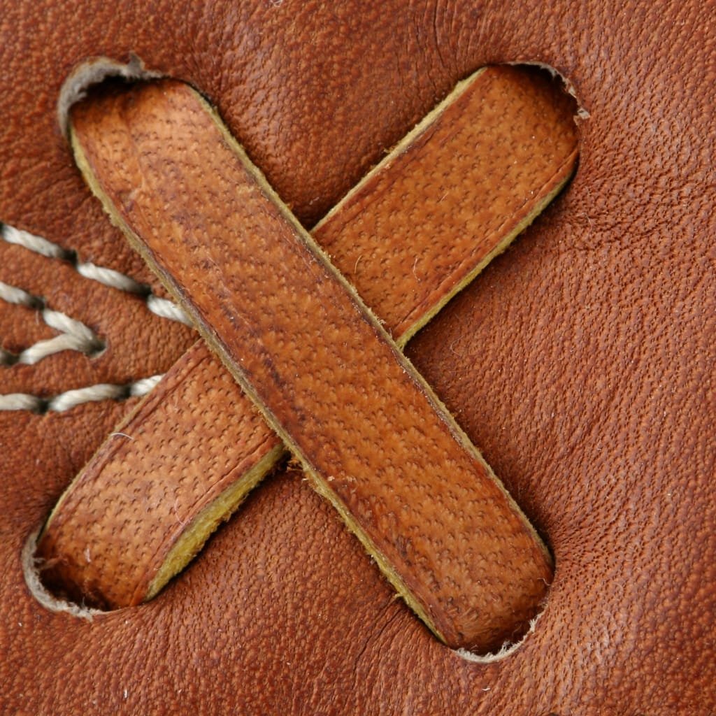 Close-up of a baseball glove's leather surface featuring a large, stitched "X" shape made of full grain leather strips.