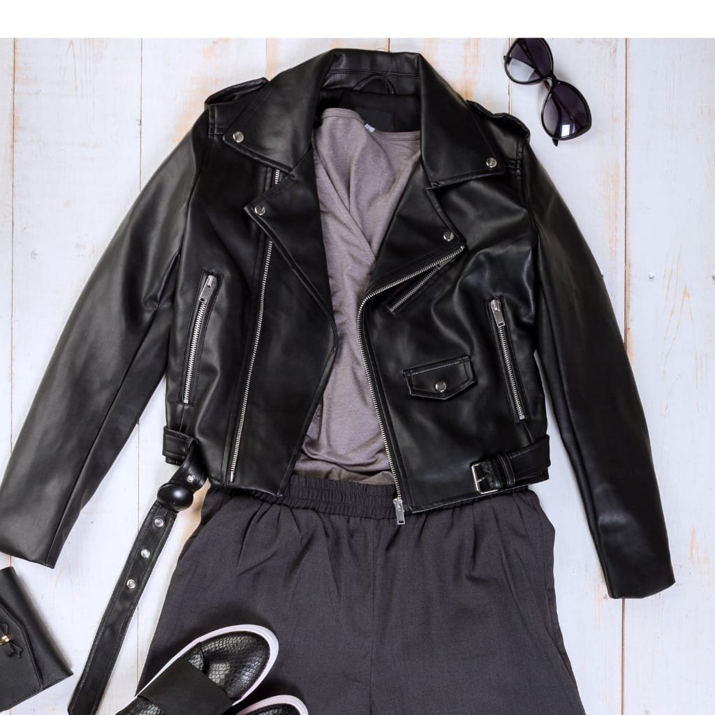 A black leather jacket with silver zippers and a grey t-shirt underneath, paired with black athletic pants and black sneakers. Sunglasses are placed at the top right corner.

