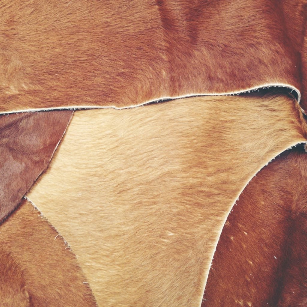 Close-up image of overlapping cowhide pieces with varying shades of brown and tan, showing the texture and natural patterns of the animal's fur.

