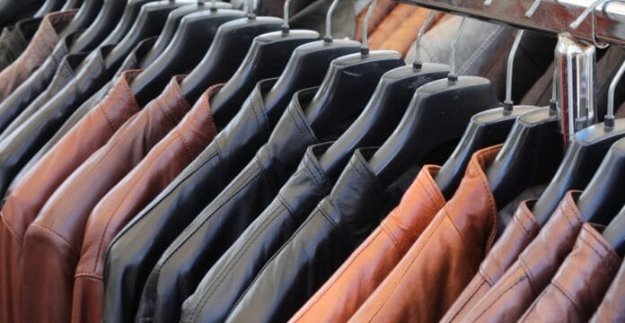 A row of cowhide leather shirt jackets hanging on black hangers on a rack, showcasing various shades including tan, black, and brown.