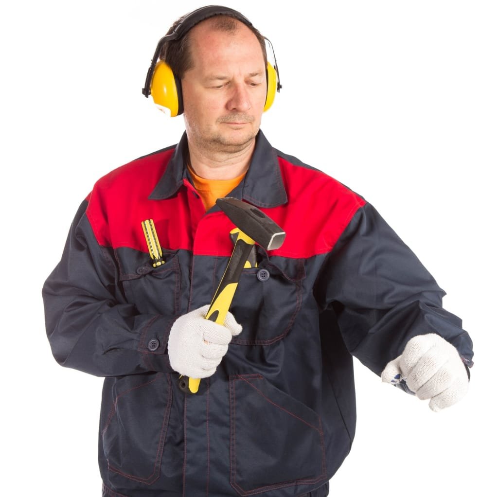 A man dressed in a workwear lined jacket, wearing yellow ear protection and gloves, holding a hammer and inspecting his sleeve.