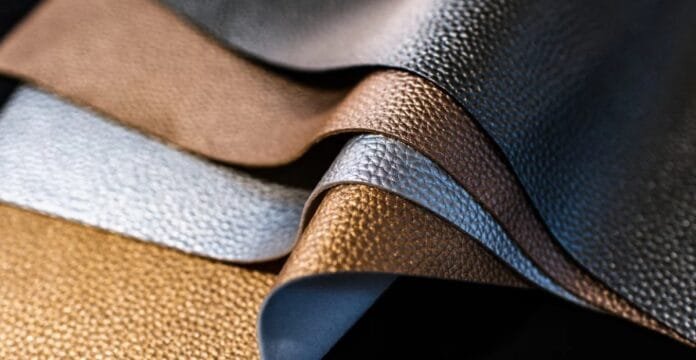 Close-up image of several textured leather fabric samples in various shades including brown, tan, white, and black, layered and arranged to showcase their surface details.