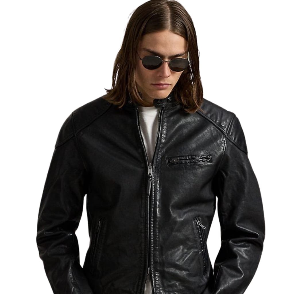 A woman with shoulder-length brown hair wearing dark sunglasses and a sleek black leather jacket, looking downward.