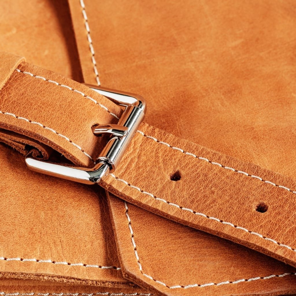 Close-up image of a tan-colored full grain buffalo leather belt with white stitching and a shiny metal buckle.

