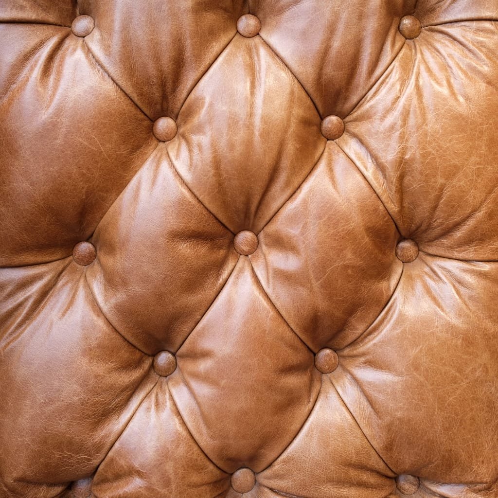 Close-up of a tufted leather upholstery with round buttons, showcasing a classic button-tufted design.
