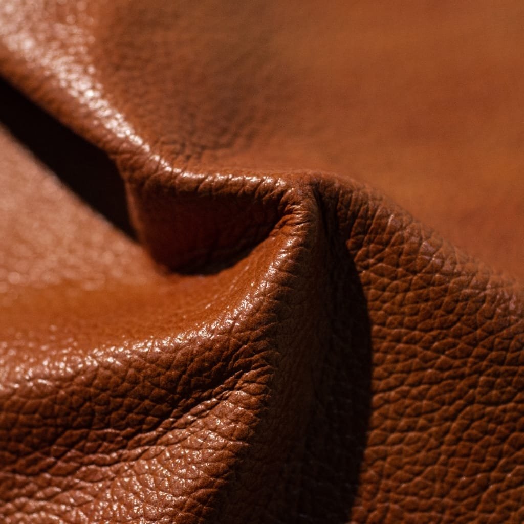 Close-up of textured brown genuine leather with visible grain and natural creases.

