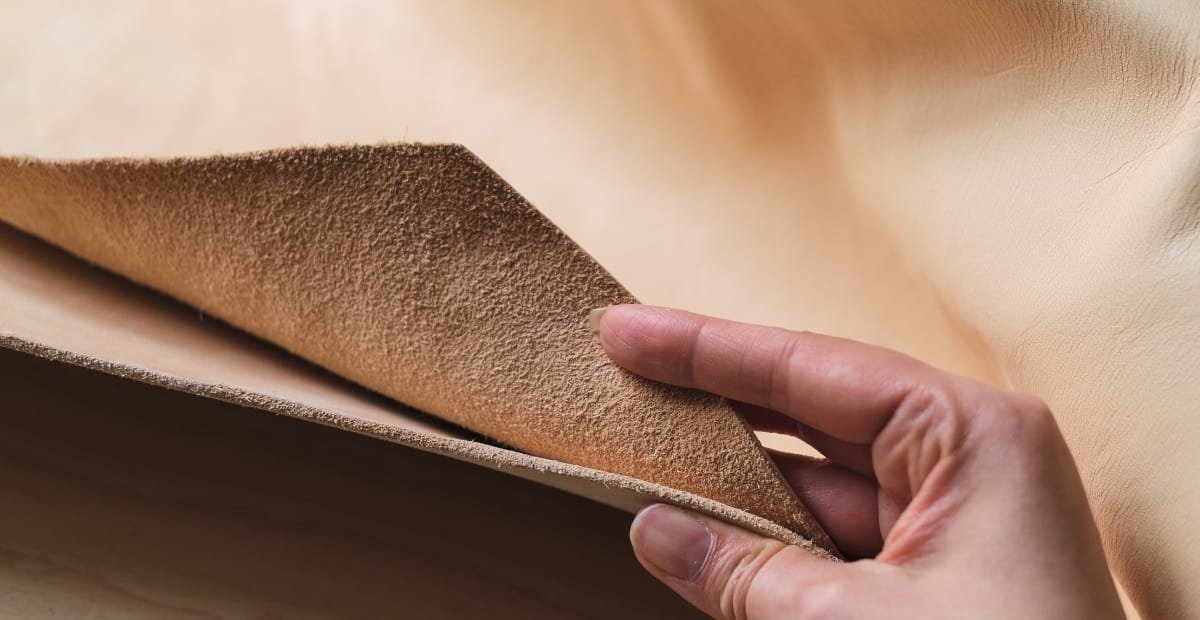 Goat Leather: The Lightweight Luxury You Need to Know About A hand lifting a piece of light brown goat leather, showing its textured surface.