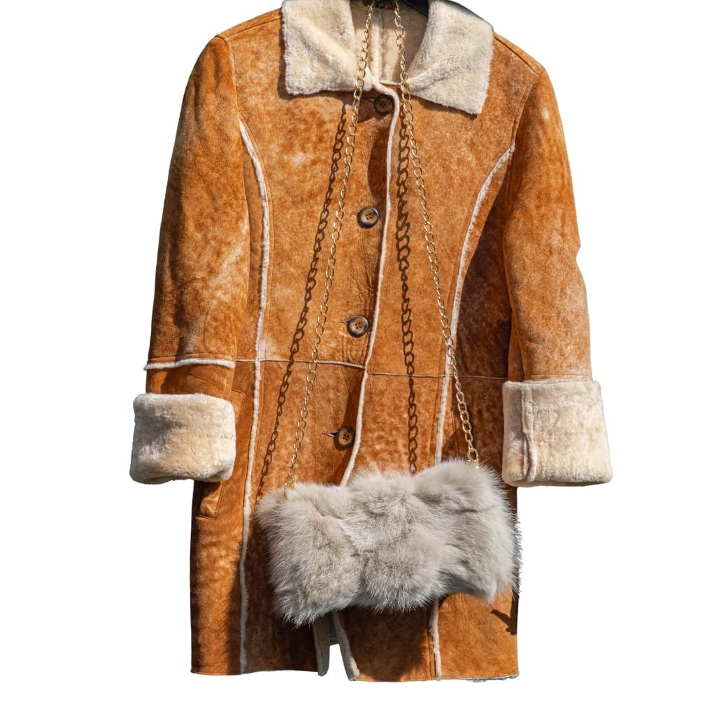 What Is a Leather Jacket? A Timeless Icon of Style and Attitude 25 A stylish goatskin jacket with a tan, shearling-lined collar, rolled-up cuffs, and visible directional stitching. It is accessorized with a fuzzy fur purse hanging from a gold chain.