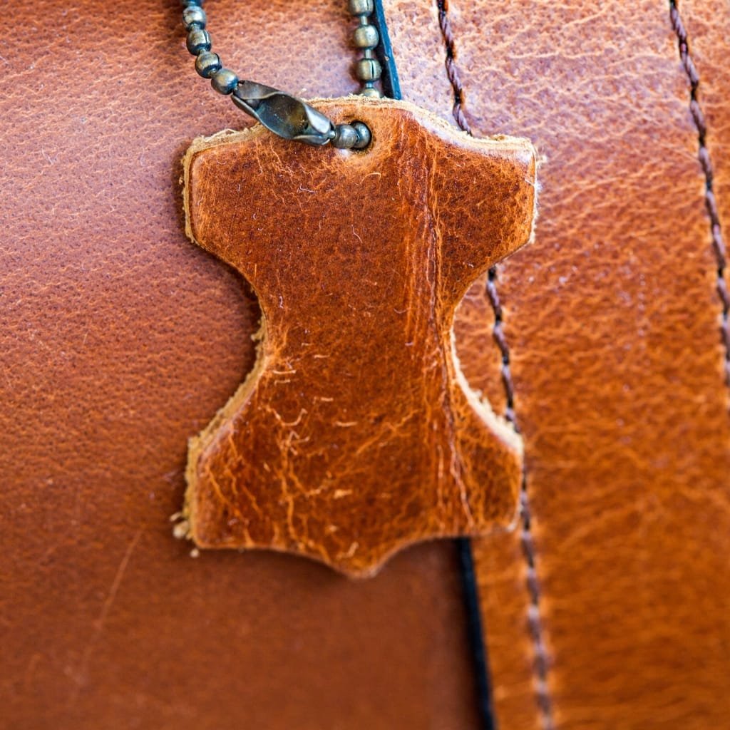 Close-up image of a brown buffalo leather piece with a leather tag attached to a beaded necklace, showcasing the texture and rich color of the leather.

