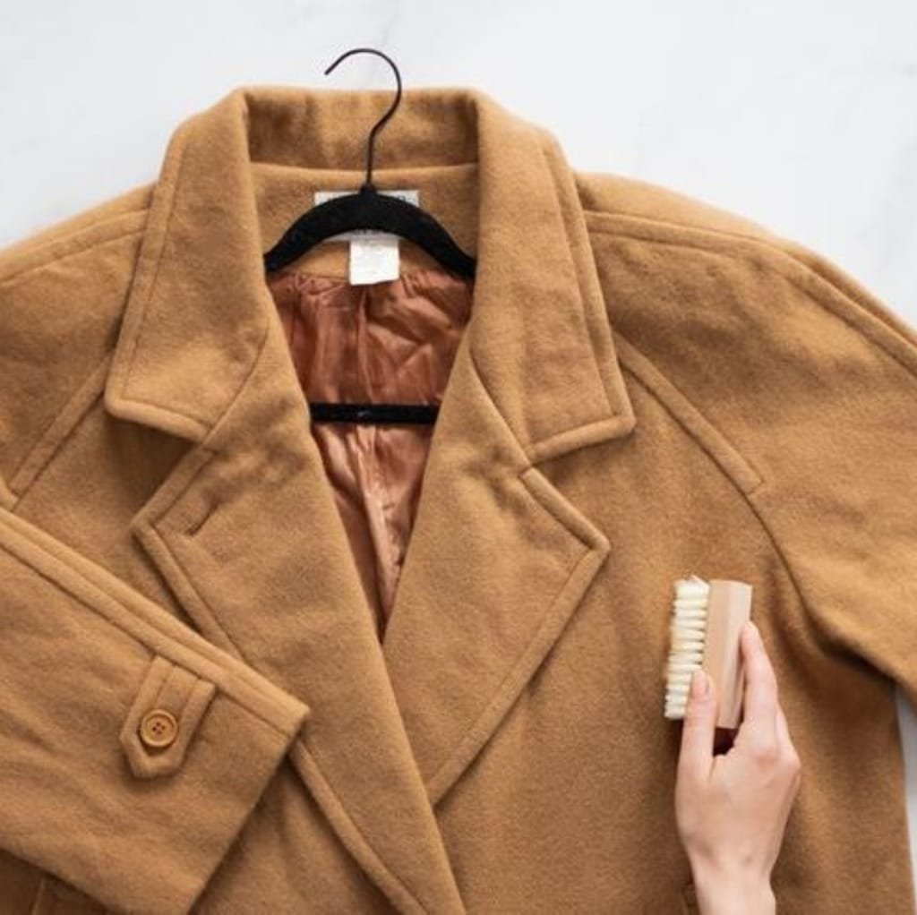 A person cleaning a camel-colored wool winter coat with a small brush.