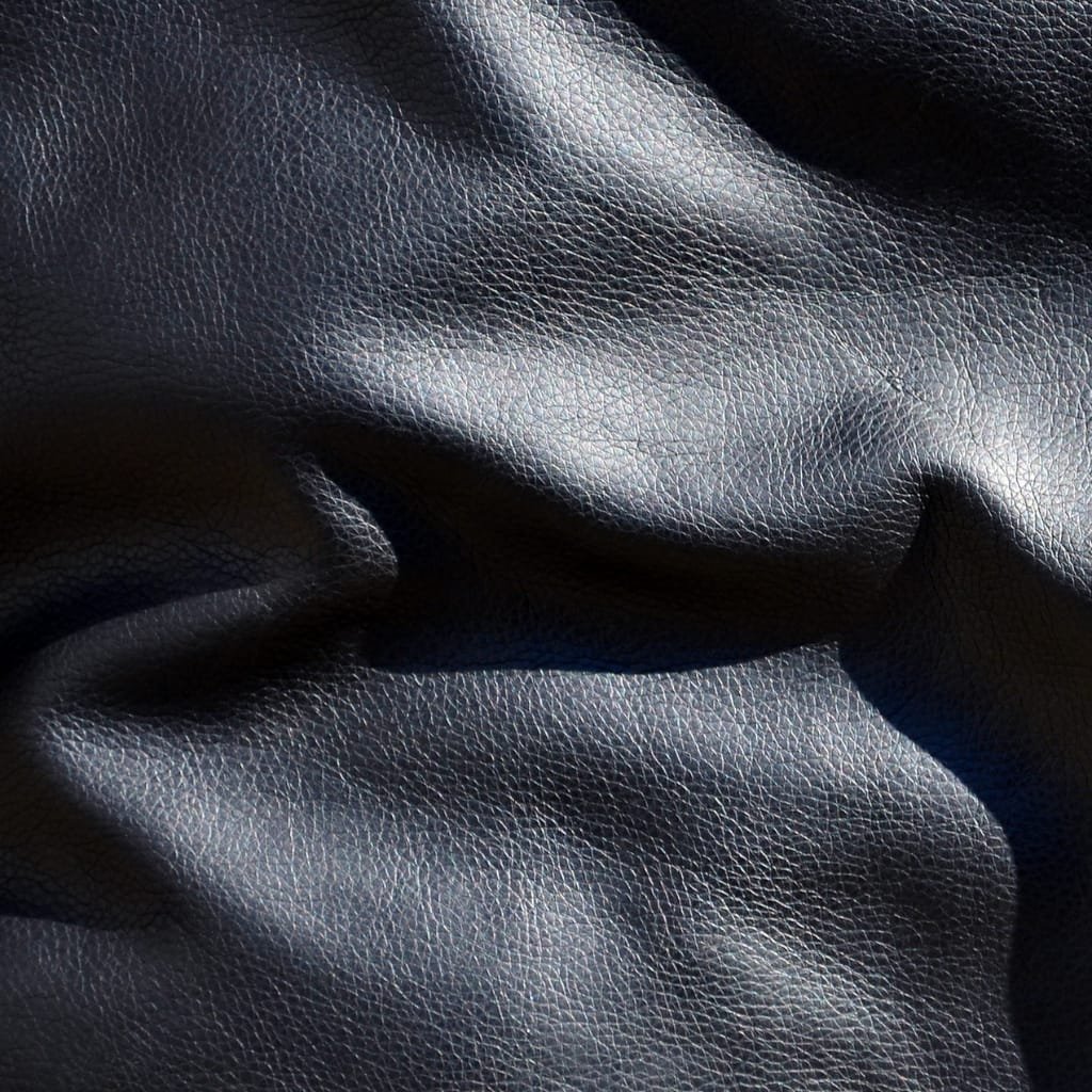 Close-up photograph of black lambskin leather fabric showcasing its fine, smooth, and slightly textured surface with soft folds and highlights.

