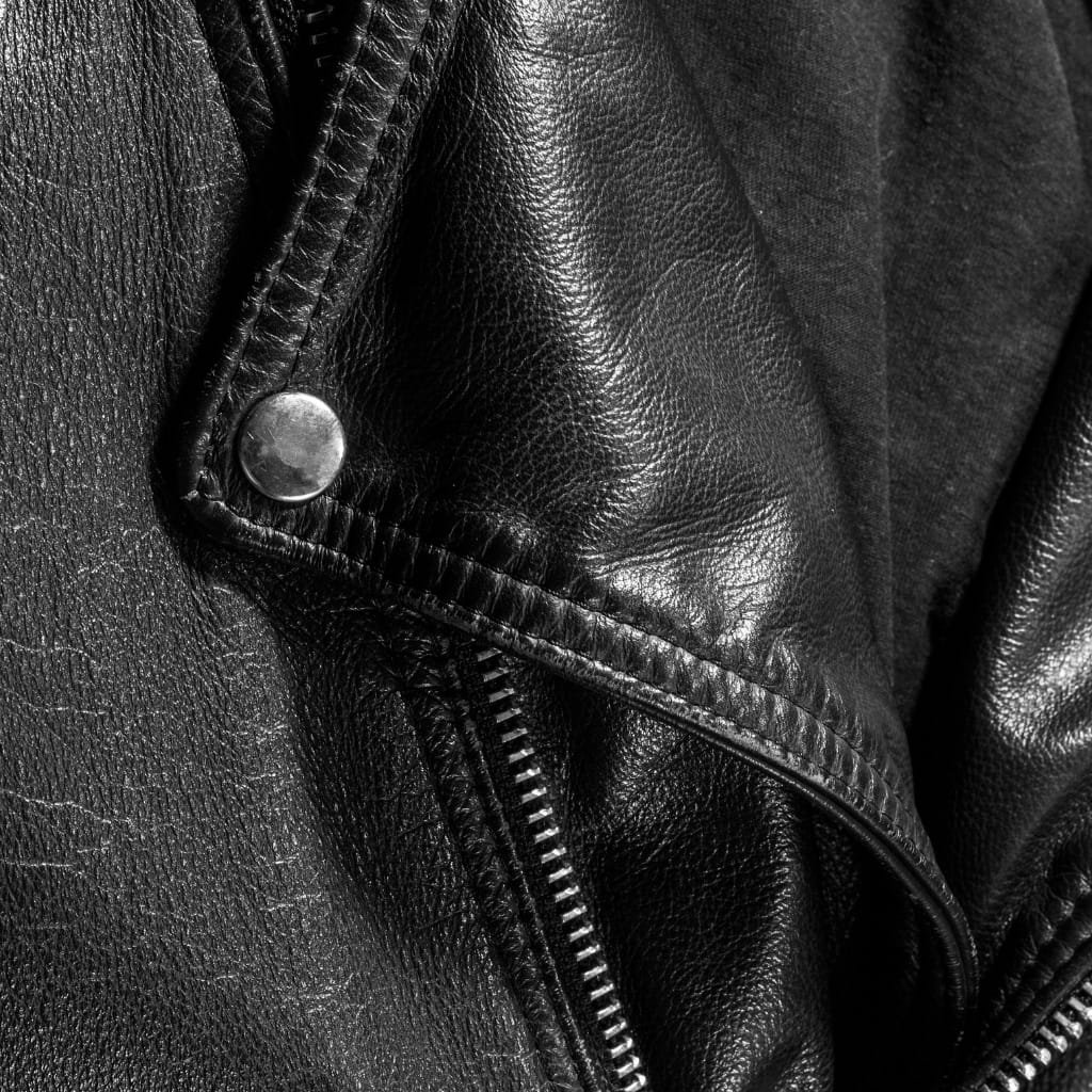 Close-up image of a black leather jacket, showing detailed texture and a silver snap button near the zipper.