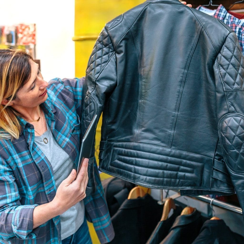 What Is a Leather Jacket? A Timeless Icon of Style and Attitude 37 A woman in a blue plaid shirt inspecting and examining a black leather jacket at a clothing store.