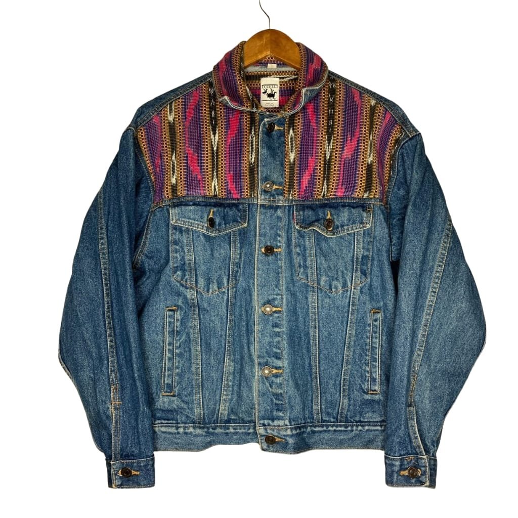 A classic blue denim jacket with a colorful, patterned woven fabric panel across the shoulders and upper chest area, displayed on a wooden hanger against a white background.