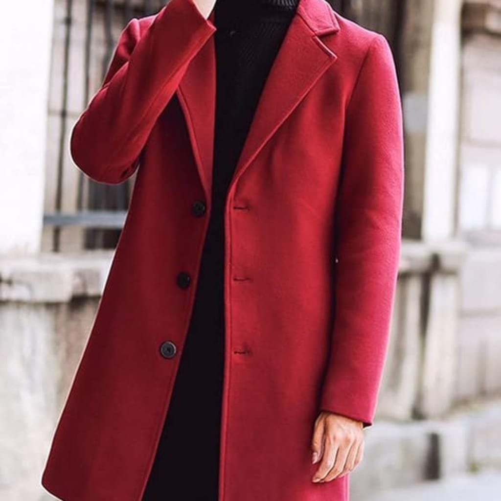 A person wearing a vibrant red, tailored pea coat with a classic lapel collar, standing outdoors in an urban setting with blurred buildings in the background.