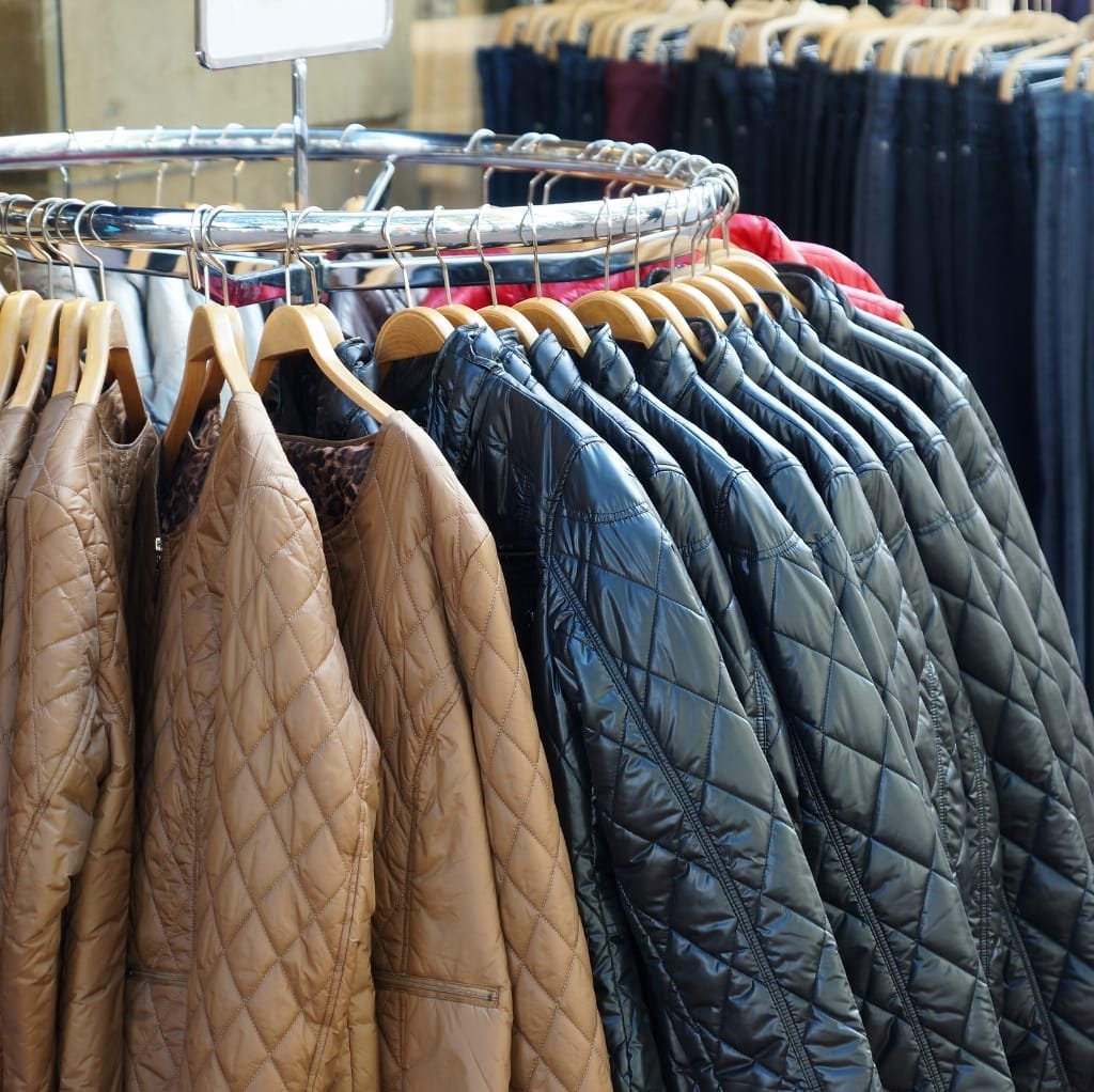 A rack of quilted bomber jackets in various colors, including tan, black, and gray, displayed on hangers in a clothing store.