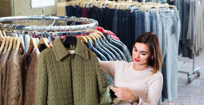 A woman shopping for clothing, holding a green quilted jacket on a hanger in a retail store.