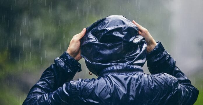 Person wearing a dark rain jacket with a hood, standing outdoors in the rain.