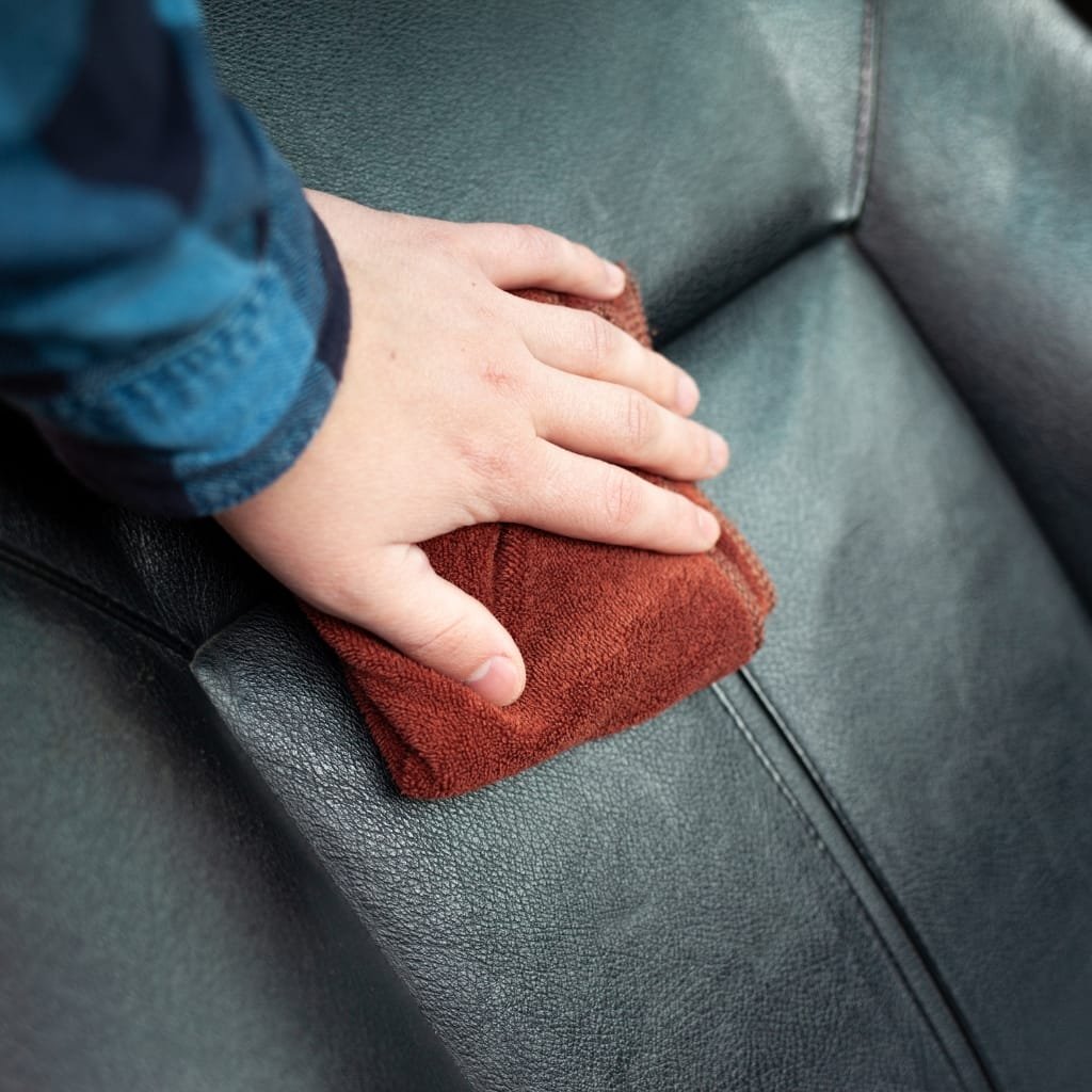 Cow’s Leather: Durable, Timeless, and Perfect for Every Style 18 A child's hand holding a red cloth while cleaning the surface of a black leather sofa.