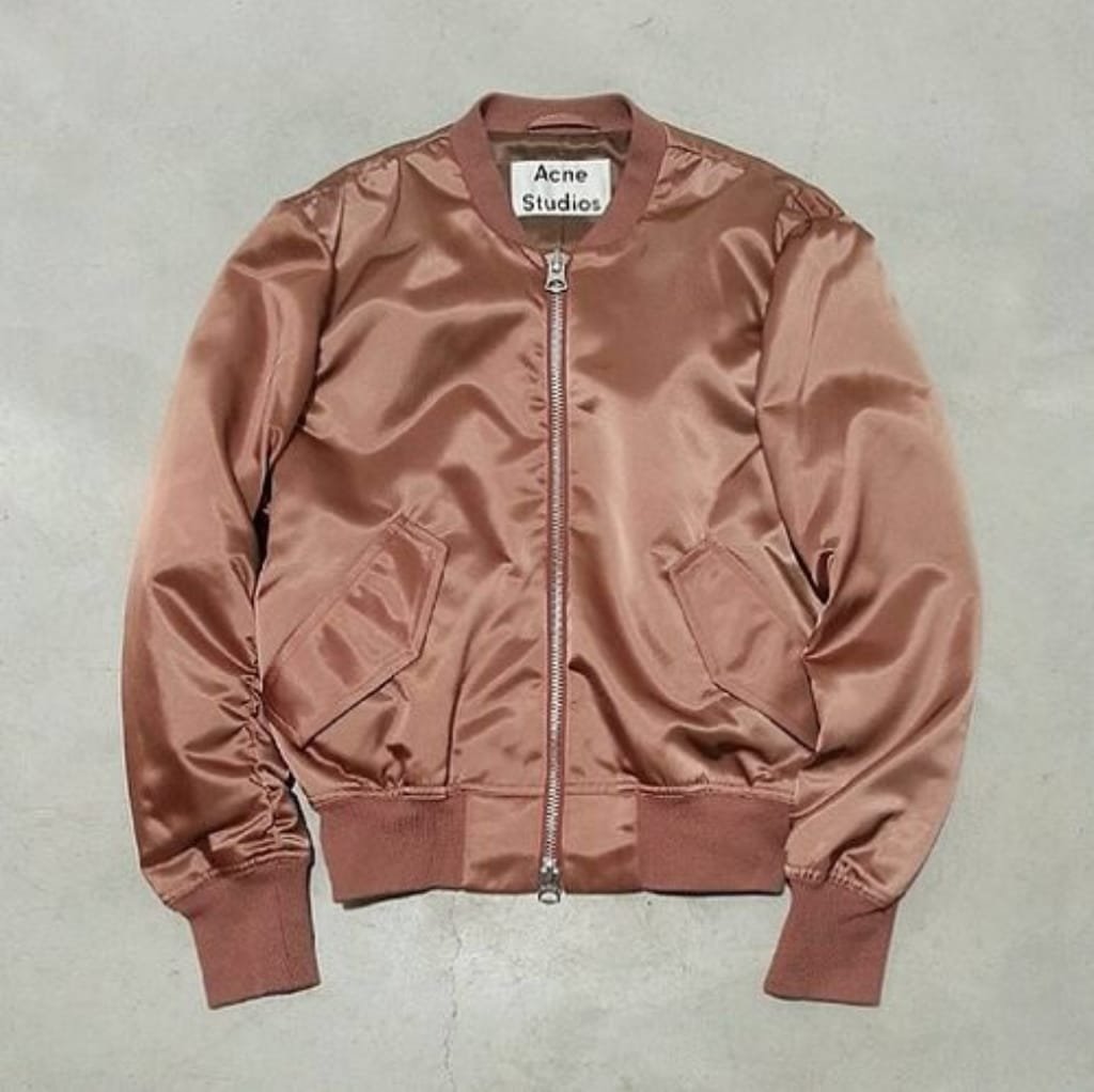 A shiny, rose-colored satin bomber jacket with ribbed cuffs and waistband, featuring two front pockets and a zipper closure, laid flat on a neutral background.