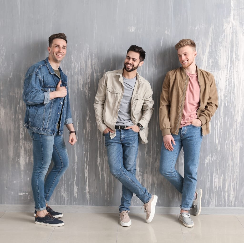 Three young men standing against a textured wall, all wearing oversized bomber jackets and casual jeans, showcasing various stylish sneakers.