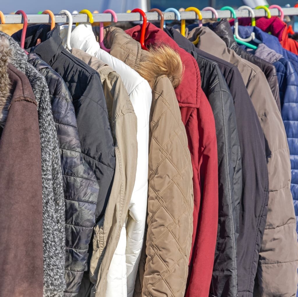 A row of winter jackets hanging on a clothing rack, featuring various colors and styles, including puffer jackets, fleece, and wool coats.