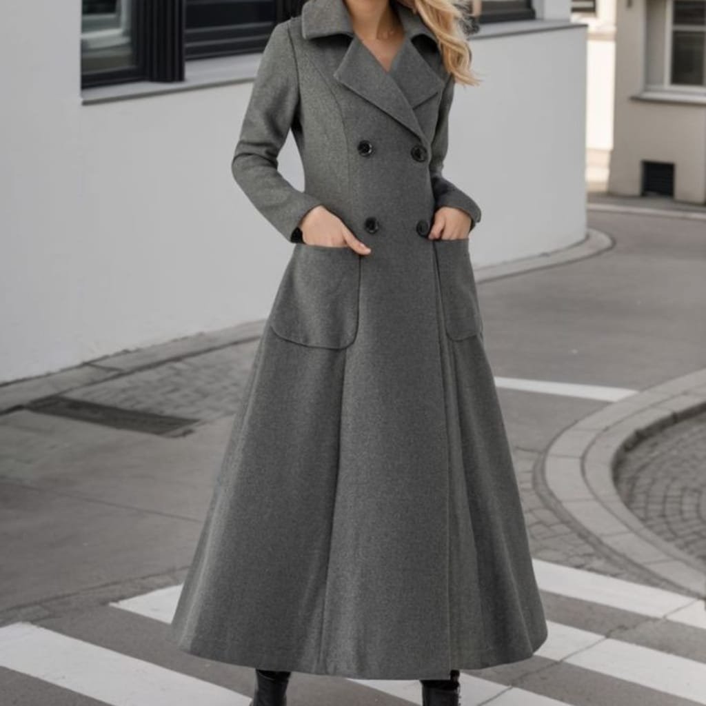 A woman standing outdoors wearing a stylish, long grey wool coat with a wide collar and double-breasted buttons. The coat has a fitted waist and large front pockets, creating a sophisticated silhouette.