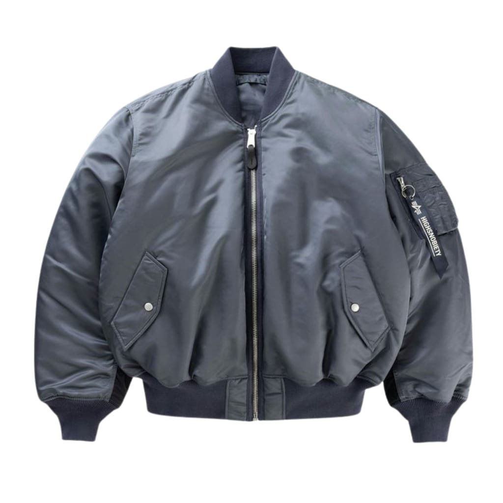 A dark gray satin bomber jacket with black ribbed cuffs, collar, and waistband, featuring a front zipper closure, two side flap pockets, and a zippered pocket with a black strap on the left sleeve.


