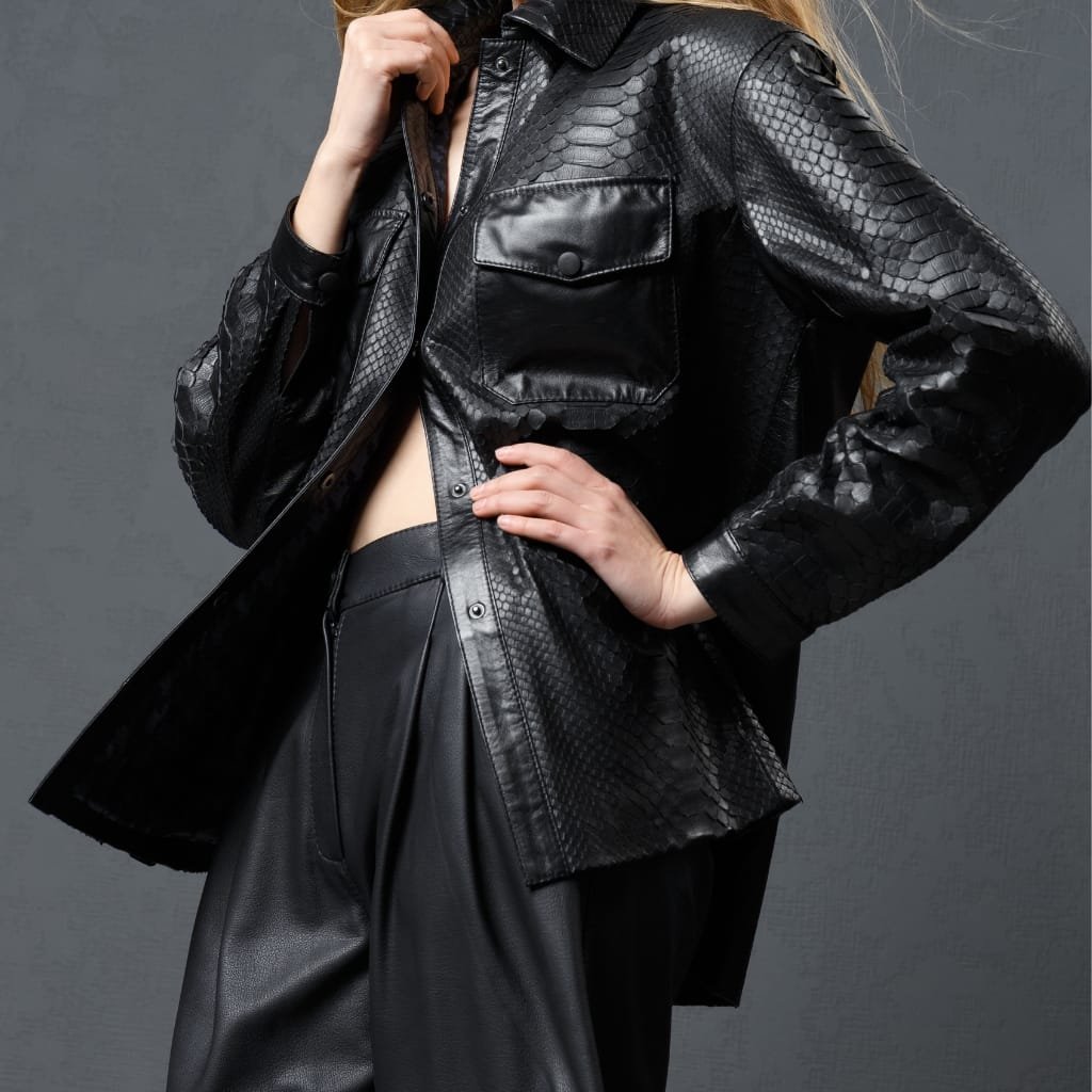 A person wearing a black leather shirt jacket with a snakeskin pattern, featuring a front pocket and button details, paired with matching black leather trousers.

