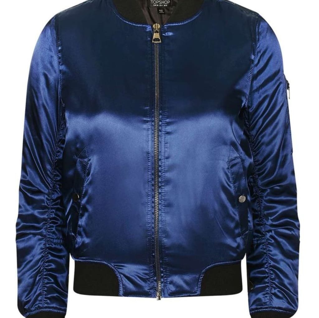 A shiny, royal blue satin bomber jacket with black ribbed cuffs and waistband, featuring a front zipper and small side pockets.