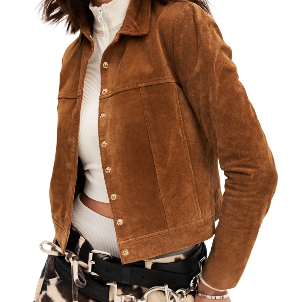 A person wearing a stylish brown suede leather jacket, paired with a white ribbed turtleneck, patterned pants, and a chain belt with accessories.