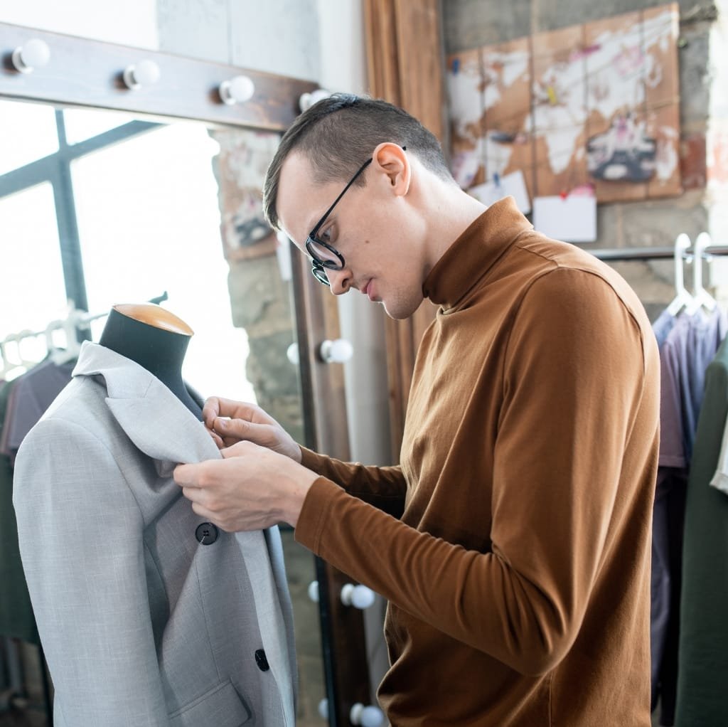 A man examining a tailored wool coat on a mannequin in a clothing store, focusing on proper fit.